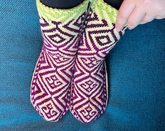 May include: A pair of hand-knitted socks with a geometric pattern in shades of purple, green, and white.