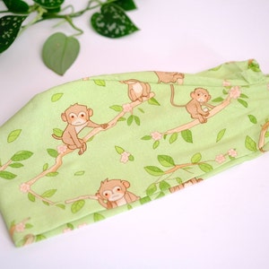 May include: A green headband with a repeating pattern of monkeys on branches with pink flowers.