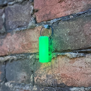 May include: A bright green cylindrical object hanging from a brick wall. The object is attached to a silver ring.