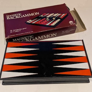 Puede incluir: Un juego de backgammon magnético vintage. El tablero es negro con triángulos naranjas y blancos. La caja burdeos muestra el nombre del juego y una imagen de las piezas. Para dos jugadores.