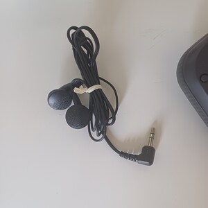 May include: Black wired earphones with a 3.5mm jack. The earphones have a black cord and a black rubber earpiece.