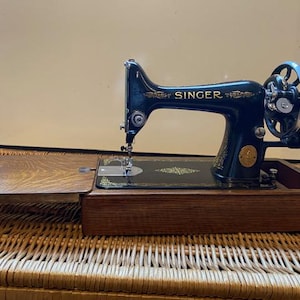May include: A vintage Singer sewing machine with a dark blue body and gold accents. The machine is in a wooden case with a hinged lid. The case is open and the machine is visible.