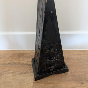 May include: A black wooden triangular box with three drawers. The box is carved with geometric designs and has a small knob on each drawer.