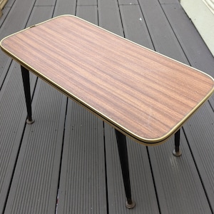 May include: A rectangular coffee table with a wood grain top and a gold-colored trim. The table has black, tapered legs. The table is approximately 30 inches long, 15 inches wide, and 18 inches tall.