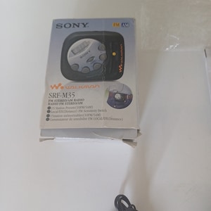 May include: A gray Sony Walkman SRF-M35 FM Stereo/AM Radio in its original box. The box features the Sony logo and the text "Walkman" in a white font. The radio has a black and silver design with a digital display and several buttons.