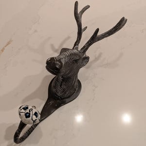 May include: A black metal deer head hook with a white ceramic knob with blue floral accents.