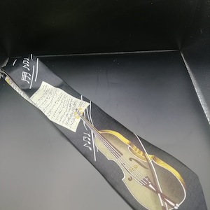 May include: Black silk tie featuring a printed image of a violin and musical notes. The tie has a white background with black musical notes and a yellow violin.
