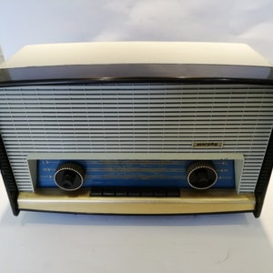 May include: A vintage Murphy radio with a black and cream colored case. The radio has a blue dial with silver knobs and a silver grill.
