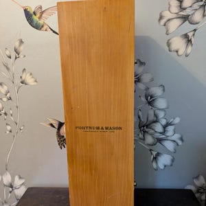Könnte beinhalten: Eine Holzkiste mit brauner Oberfläche und dem aufgedruckten Text "Fortnum & Mason, Piccadilly, London, W1A 1DE" auf der Vorderseite.