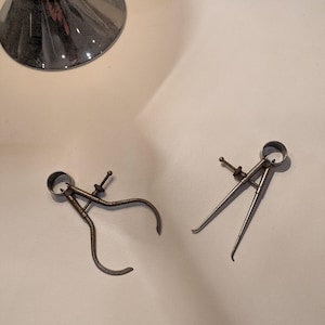 May include: Two silver metal calipers, one with a closed ring and the other with an open ring, on a white surface.