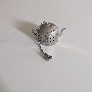 May include: Silver teapot-shaped tea infuser with a chain and a bell-shaped end.