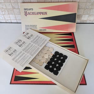 Puede incluir: Un juego de backgammon vintage con un tablero de madera, fichas blancas y negras y dados. La tapa de la caja presenta el nombre del juego, "Spear's Backgammon", en letras negras y rojas.