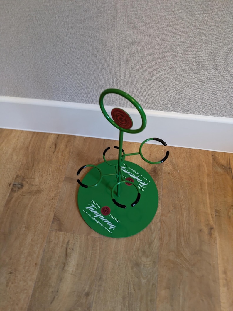 Pode incluir: Porta-copos de metal verde com an&eacute;is pretos e um logotipo Tanqueray. O porta-copos &eacute; projetado para segurar seis copos.