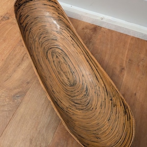 Op de afbeelding: Een grote, ovale houten kom met een bruin en zwart swirl-patroon. De kom is gemaakt van geweven hout en heeft een gladde, gepolijste afwerking.