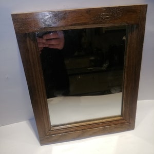 Könnte beinhalten: Ein rechteckiger Spiegel mit einem braunen Holzrahmen. Der Spiegel hat ein schlichtes Design mit einer glatten Oberfläche.