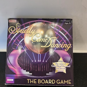 以下が含まれることがあります： ディスコボールのグラフィックが特徴の「Strictly Come Dancing」のボードゲームボックス。紫色の箱には「The Board Game」と「With the voice of Craig Revel Horwood and Strictly theme」の文字が記載されています。