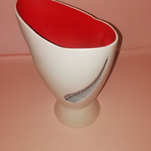 Könnte beinhalten: Eine weiße Keramikvase mit rotem Innenraum und einem schwarzen Federdesign. Die Vase hat eine breite Öffnung und einen schmalen Boden.