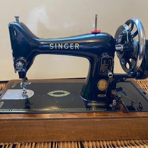 May include: A vintage Singer sewing machine in black and gold with a wooden case. The machine has a hand crank and a foot pedal.