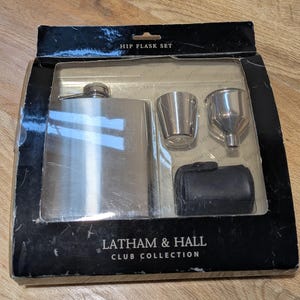 May include: A silver hip flask set with a funnel and a shot glass. The set is packaged in a black box with the words "HIP FLASK SET" and "LATHAM & HALL CLUB COLLECTION" printed on it.