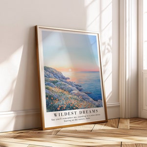 Puede incluir: Una impresión enmarcada con una pintura de acuarela de una costa rocosa con una puesta de sol sobre el océano. La impresión tiene el texto "WILDEST DREAMS" y el texto "Say you'll remember me, standing in a nice dress Staring at the sunset, babe".