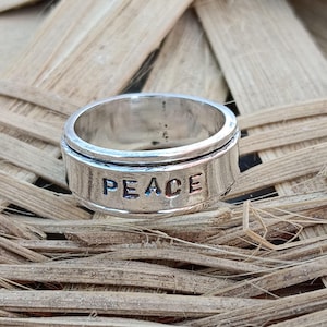 May include: A silver spinning ring with the word "PEACE" engraved on the band.