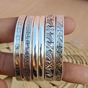 May include: A set of silver bangles with different engraved designs, including stars, geometric patterns, and floral motifs.