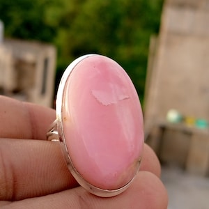 Op de afbeelding: Zilveren ring met een grote, ovale roze edelsteen. De edelsteen heeft een glad, gepolijst oppervlak met een kleine imperfectie. De ring heeft een eenvoudig ontwerp dat de edelsteen benadrukt. Een sieraad.
