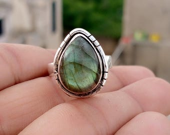 May include: A silver ring featuring a pear-shaped, iridescent green gemstone. The stone is set in a detailed, textured bezel. The ring's band is a simple, polished silver. The gemstone displays shades of green and blue.