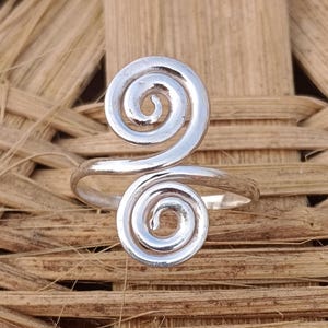 May include: A silver ring featuring a double spiral design. The ring is crafted from smooth, shiny metal and has a simple, elegant style.