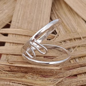 May include: A silver ring with a unique, abstract design. The ring is open on one side and has a curved shape.