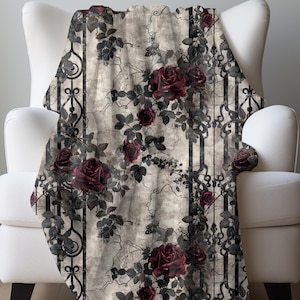 May include: A soft throw blanket featuring a repeating pattern of deep burgundy roses and dark green leaves intertwined with black wrought iron-style vertical scrollwork against a textured, light beige and grey distressed background.