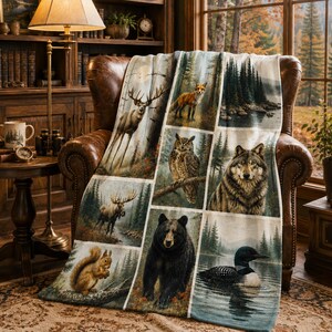 May include: A soft throw blanket featuring a grid of wildlife illustrations including a deer, fox, owl, wolf, moose, squirrel, black bear, and loon, all set against a backdrop of forest and lake landscapes in natural earth tones.