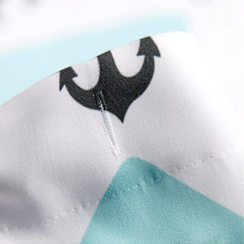 May include: Close-up of a white fabric with a black anchor print and a turquoise blue geometric pattern. The fabric has a white seam running down the center.