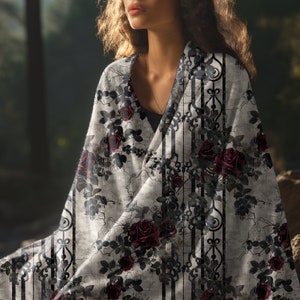 May include: A lightweight fabric wrap featuring a pattern of deep red roses and dark green leaves intertwined with black vertical ornate scrollwork lines against a textured light grey background, draped over the shoulders to cover the upper torso.