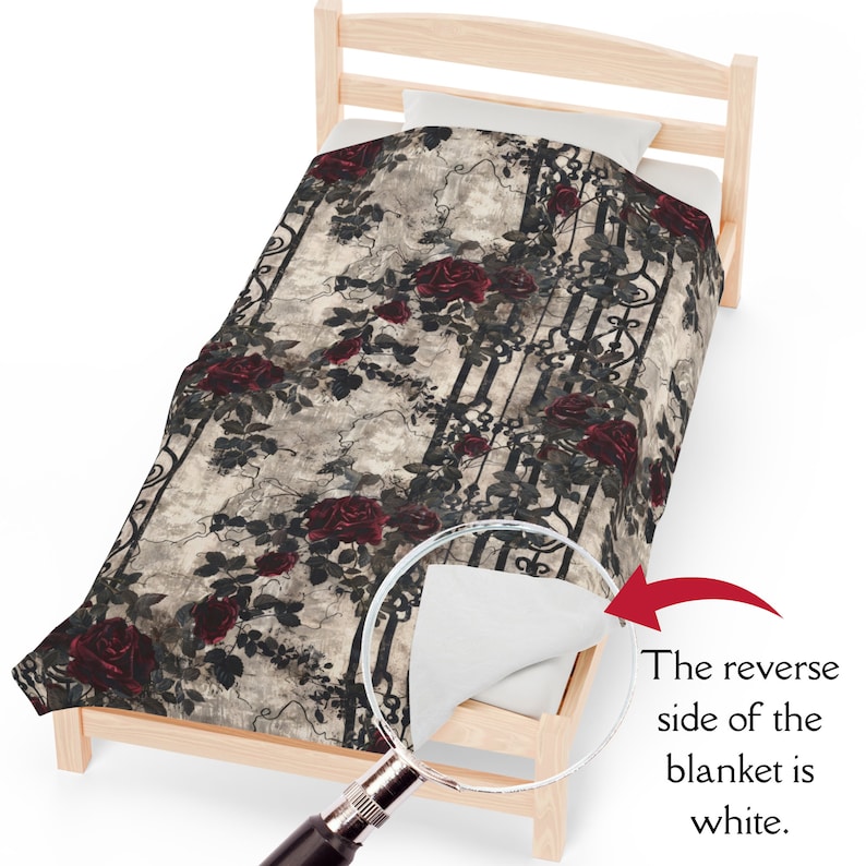 May include: A blanket featuring a pattern of dark red roses and black wrought iron gate designs on a textured beige background. A magnifying glass highlights a corner of the blanket, revealing a plain white reverse side with the text: The reverse side of the blanket is white.
