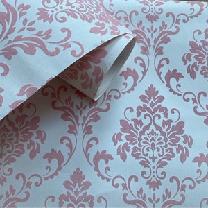 Puede incluir: Rollo de papel tapiz con estampado damasco rosa. El papel tapiz tiene un fondo blanco con un dise&ntilde;o floral rosa.