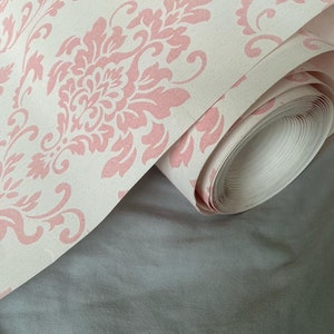 Puede incluir: Un rollo de papel tapiz con estampado damasco en rosa y blanco.