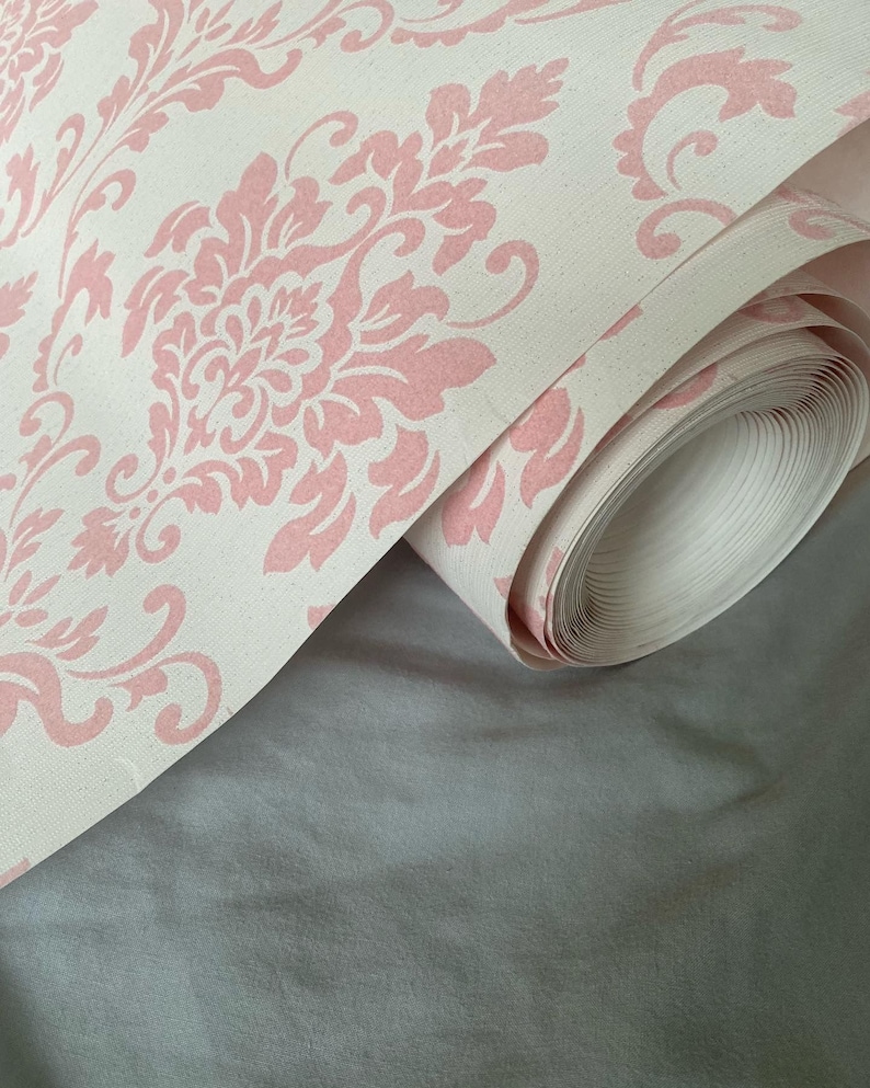 Puede incluir: Un rollo de papel tapiz con estampado damasco en rosa y blanco.