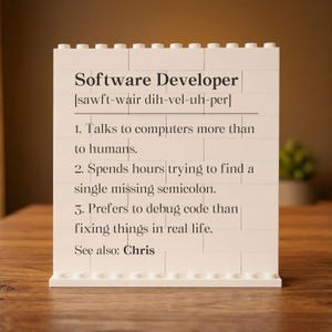 May include: A white brick-style sign with the text "Software Developer" and a phonetic pronunciation guide. The sign lists humorous characteristics of software developers, including preferring computers to humans and debugging code. The text "See also: Chris" is at the bottom.