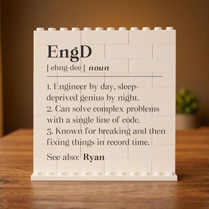 May include: A white brick-style sign with the word "EngD" in black, followed by a definition. The definition includes the phrases "Engineer by day, sleep-deprived genius by night" and "fixing things in record time."