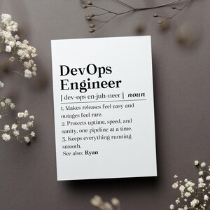 May include: A white card with the text "DevOps Engineer" and its pronunciation. The card defines the role, highlighting its functions: making releases easy, protecting uptime, and keeping things running smoothly. The card is on a gray surface, decorated with white flowers.