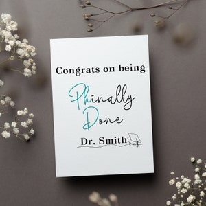 May include: A white card with black text that reads "Congrats on being Finally Done Dr. Smith" with a small black graduation cap illustration.