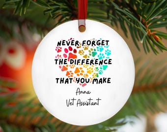 May include: White round Christmas bauble with a rainbow paw print heart design. The bauble reads "Never forget the difference that you make."  The text "Anna Vet Assistant" is printed below the heart.