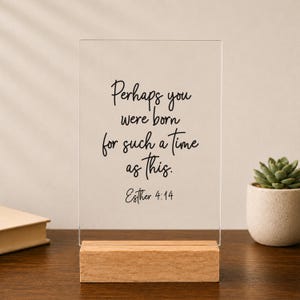 May include: A rectangular clear acrylic sign standing on a light-colored wooden base. The sign features black cursive text that reads: Perhaps you were born for such a time as this. Esther 4:14. The sign is positioned upright on a flat surface.