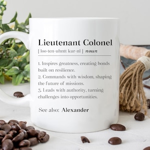 May include: White ceramic mug with the definition of "Lieutenant Colonel" printed in black. The definition includes the pronunciation, the word "noun", and three bullet points describing the role. The text "See also: Alexander" is also included.