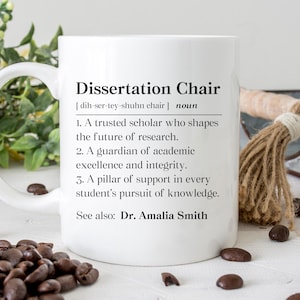 May include: White ceramic mug with the text "Dissertation Chair" and its definition. The definition includes three points about a trusted scholar, guardian, and pillar of support. The mug also includes "See also: Dr. Amalia Smith". Coffee beans are scattered around the mug.
