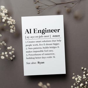 May include: A white card with the text "AI Engineer" and its pronunciation, along with a definition. The card is on a gray surface, decorated with white flowers and a twig.