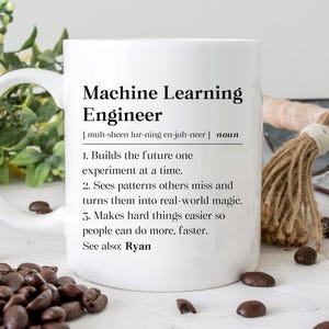 May include: White ceramic mug with the text "Machine Learning Engineer" and a definition. The mug also lists the definition of the job. Coffee beans are scattered around the mug.