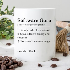May include: White ceramic mug with the text "Software Guru" and a definition. The definition includes: debugs code like a wizard, speaks fluent binary and sarcasm, and turns caffeine into magic. The mug is surrounded by coffee beans.