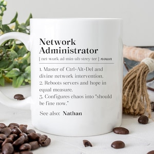 May include: A white ceramic mug with a large handle, featuring the text "Network Administrator" and a humorous definition. The mug is surrounded by coffee beans and decorative elements, suggesting a gift or novelty item.